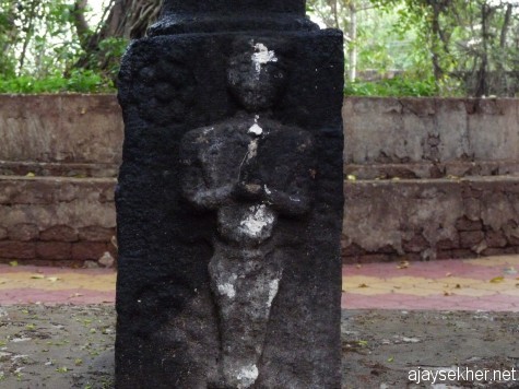 Tozhuvan figure at the base of the stone lamp post before the Tozhuvanur temple, Kavumpuram, Walanchery.  It is similar to the Siddha idol of Kayikara in posture and in attire.